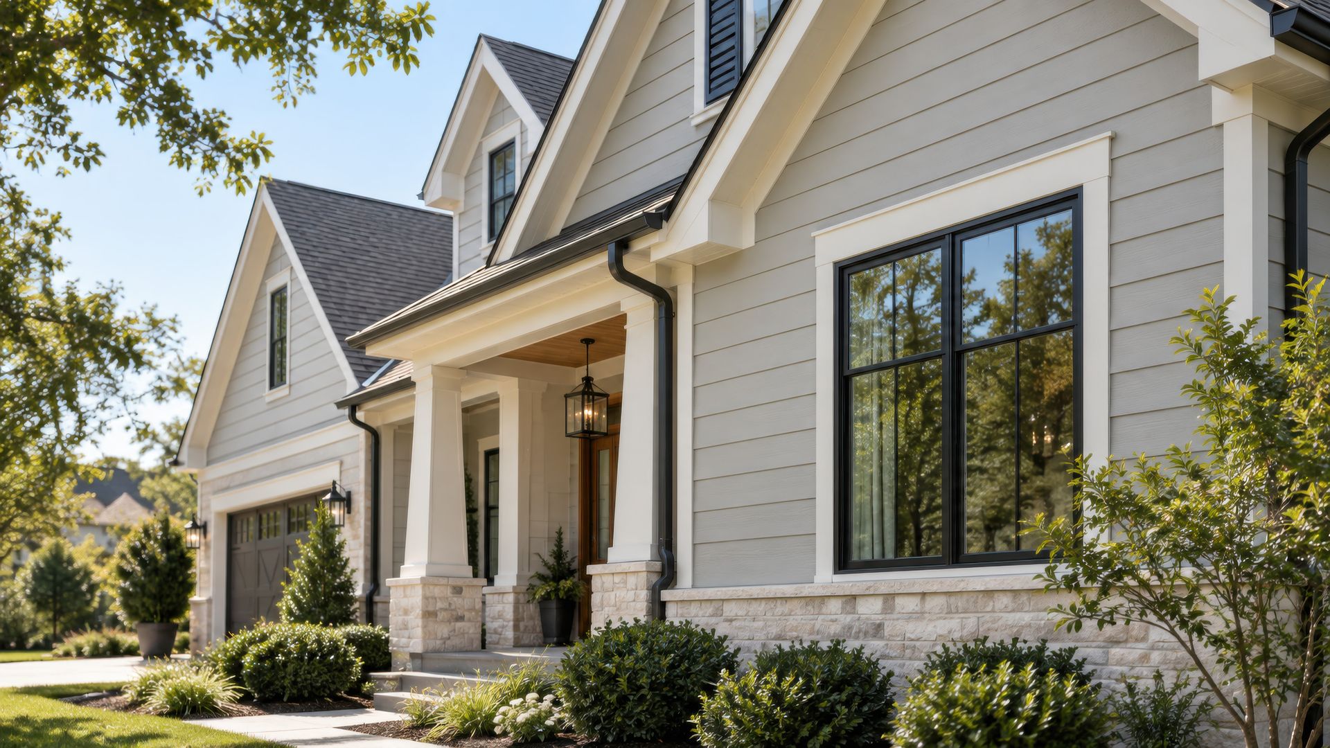 A home with light grey fiber cement lap siding, white trim, black windows and a stone base